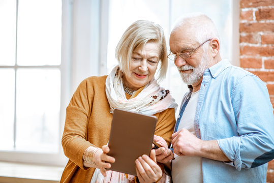 Beautiful senior couple using digital tablet standing together near the window at home - Powered by Adobe