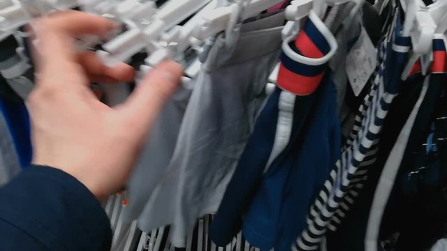 The man in the store chooses underwear panties. The person touches a boxers. There is a large selection of shorts in various colors. A male with his hand considers different types of cotton male brief