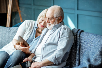 Lovely senior couple dressed casually using digital tablet while sitting together on the...