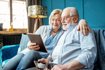 Lovely senior couple dressed casually using digital tablet while sitting together on the comfortable couch at home