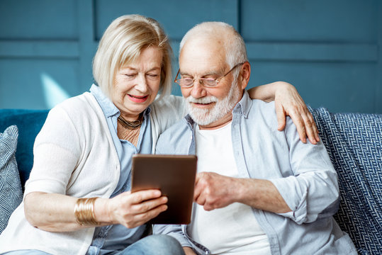 Lovely senior couple dressed casually using digital tablet while sitting together on the comfortable couch at home