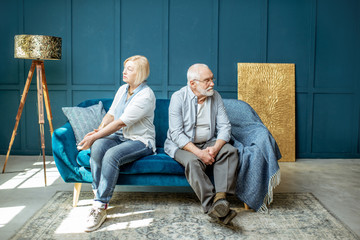 Offended senior man and woman feeling sad, sitting back to each other on the couch at home