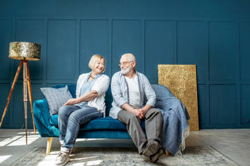 Lovely senior couple sitting together on the couch in the living room at home, wide interior view