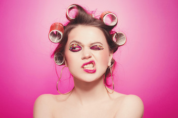 Cheeky girl posing on pink background in body, with curlers on head. Pretty woman with sweet makeup in studio