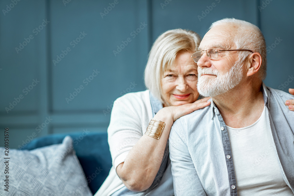 Wall mural portrait of a beautiful senior couple embracing each other, sitting on the couch at home