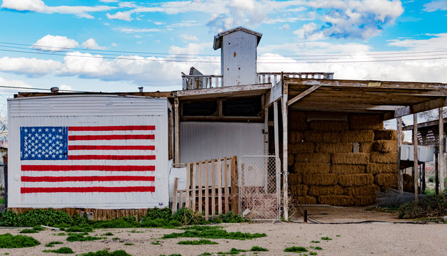 American flag graffiti on old white house with hay