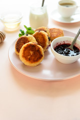 Cottage cheese pancakes with blueberry, honey, jam and coffee. Ukrainian syrniki, cottage cheese fritters or pancakes on pink wooden background. Healthy eating concept. Selective focus