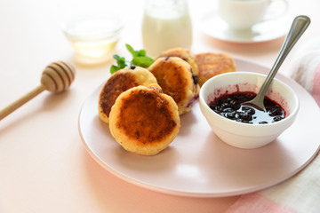 Cottage cheese pancakes with blueberry, honey, jam and coffee. Ukrainian syrniki, cottage cheese fritters or pancakes on pink wooden background. Healthy eating concept. Selective focus