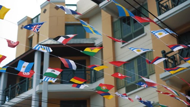 A string of small national flags waving in the air on the city street in the daytime at summer