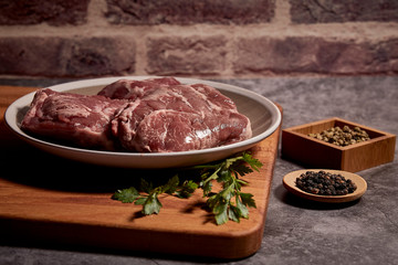 pork cheeks on a plate on a wooden board and next to different spices