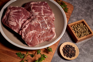 pork cheeks on a plate on a wooden board and next to different spices