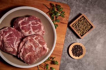 pork cheeks on a plate on a wooden board and next to different spices