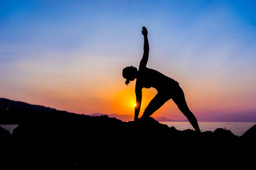 Silhouette of a young woman doing yoga on the beach at sunset.