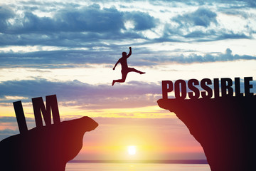 Man jumping over impossible or possible over cliff on sunset background