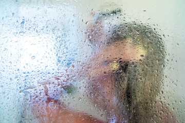 woman in the shower behind glass with drops