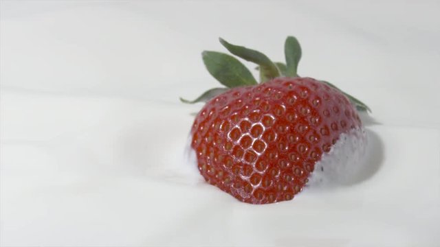 Slow motion close-up shot of a straberry falling into cream. Shot on Red