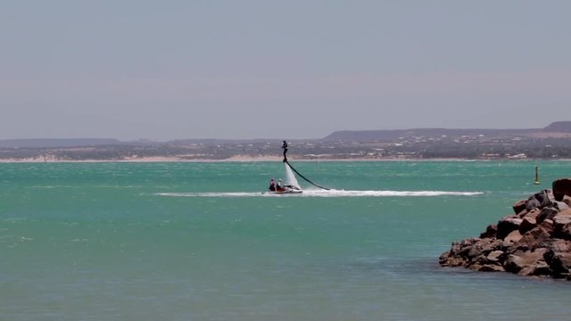 Drone shot over the ocean of a person riding a flyboard behind a jet ski.