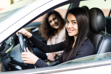 Two attractive friendly young women enjoying a day trip to town viewed through the open window of their car grinning happily at the camera