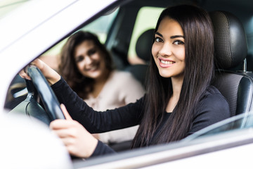 Two attractive friendly young women enjoying a day trip to town viewed through the open window of their car grinning happily at the camera