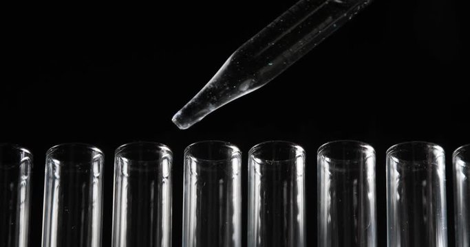 Pipette drips two drops of clean chemicals into the each test tube in the row on black background. Chemical and medicine concept. Close-up view.