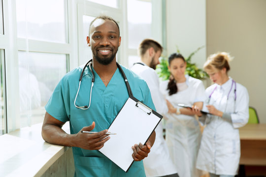 Beautiful smiling male professional doctor standing over hospital background. African american man showing empty banner with copyspace. Advertising image about healthcare, health, clinic, medicine.