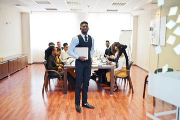 Face of handsome african business man, holding laptop on the background of business peoples multiracial team meeting, sitting in office table.