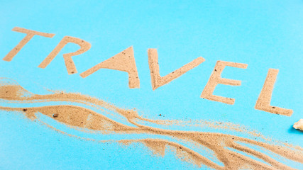 The word travel written on a bright blue background of beach sand - a vacation at sea concept. Top view, flat lay