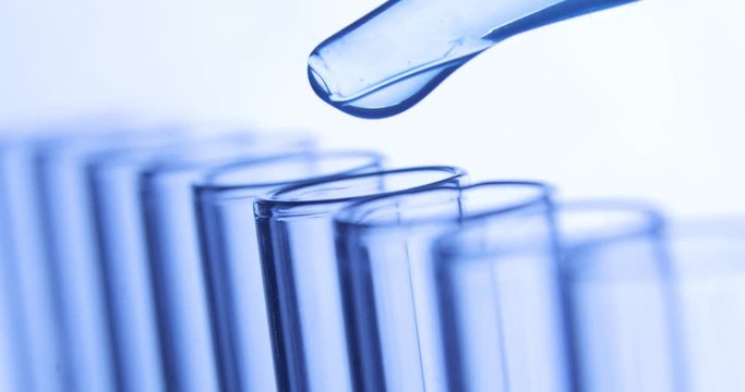 Laboratory research testing. Pipette drips drops of blue clean water into test tubes. Chemical and medicine concept. Close-up side view.