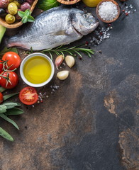 Raw dorado fish with spices and vegetables on the graphite board.