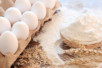 Wheat flour in a Cup on the table. Eggs and wooden objects of peasant life. Ingredients for making bread or baking.