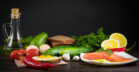 red fish, fried egg with bread and tomatoes .cucumbers, avocado, sprinkle, garlic, oil on a wooden background