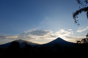 the view of the sun rises from behind the mountain, with a blue cloud background