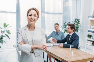 Fototapeta premium selective focus of cheerful woman standing with crossed arms near coworkers