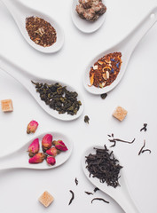 Different variety of dry tea in white spoons on the white background