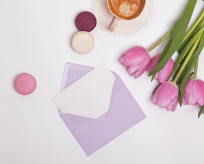 Envelope wih blank paper card on the table with pink tulips and coffee