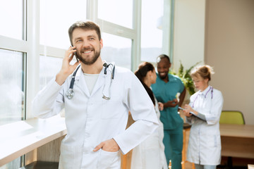 Healthcare people group. Professional caucasian male doctor with phone posing at hospital office or...