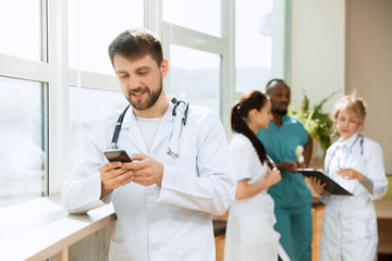 Healthcare people group. Professional caucasian male doctor with phone posing at hospital office or clinic. Medical technology research institute and doctor staff service concept. Happy smiling models - Powered by Adobe