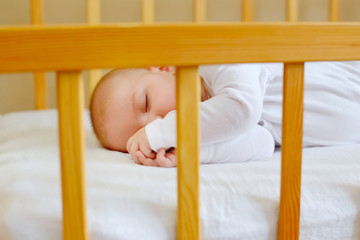 Portrait of a beautiful little boy 5 months old in white clothes, sleeping in his crib. Childhood dreams. Concept of health and children. Selective focus.