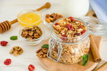Multicereal homemade organic granola with a mixture of nuts, dried cherries, honey, cinnamon  and yogurt in a glass jar on a white wooden background.