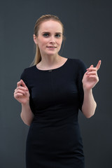 Studio portrait concept of a beautiful fashionable blond business girl standing and talking in a business dress against a gray background.