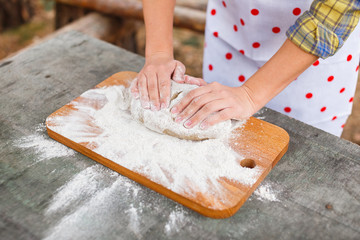 The girl in a white apron prepares the dough on a cutting board
