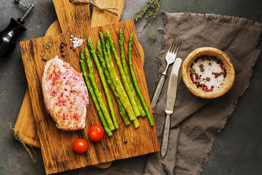 Flat lay grilled chicken breast, asparagus, cherry tomato, spices on cutting boards, dark background. View from above,overhead