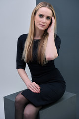 Fototapeta premium Studio portrait concept of a beautiful fashionable blond business girl sitting and talking in a business dress against a multicolored background.