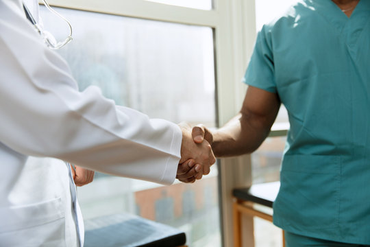 Deal. Concept of collaboration in medicine. Close up photo of two doctors shaking hands on gray hospital background. Advertising image about healthcare, health, clinic, medicine and teamwork.