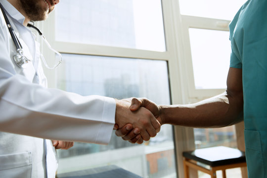 Deal. Concept of collaboration in medicine. Close up photo of two doctors shaking hands on gray hospital background. Advertising image about healthcare, health, clinic, medicine and teamwork.