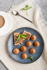 Chocolate truffle with piece of milk chocolate on blue ceramic plate on gray concrete background.