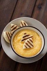 Bowl of polenta with grilled cheese, high angle view on a rustic wooden background, studio shot