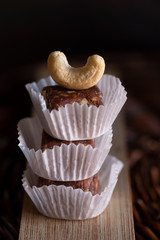 Natural vegan organic sweets made of dried fig, cashew nuts and peanut. Fruit and nuts candy bars in paper molds with the whole cashew nut on the top on wooden board and wicker tray.