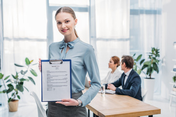 selective focus of happy recruiter holding clipboard with resume cv lettering near coworkers