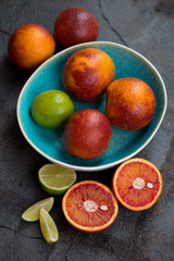 Whole and sliced sicilian blood oranges and limes over grey stone background